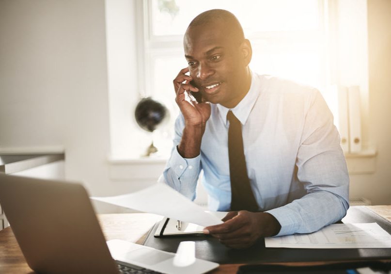 Smiling businessman reading paperwork over the phone and working